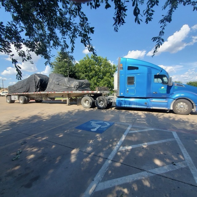 Blue Kenworth tractor hooked to a flatbed carrying tarped industrial machinery on a Badass Logistics project move