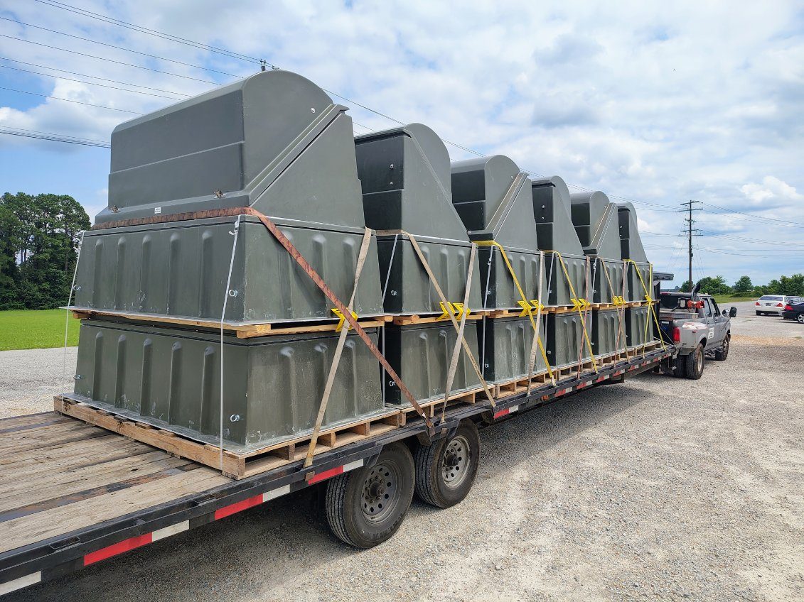 Row of large grey industrial dust collectors strapped down on a gooseneck flatbed by Badass Logistics