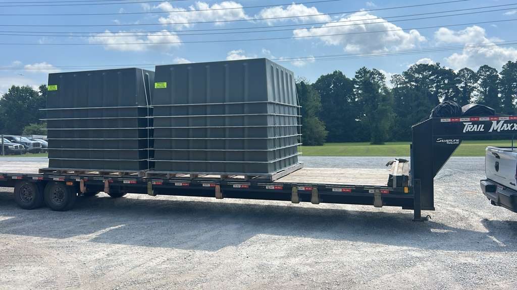 Grey industrial enclosures loaded low on a gooseneck flatbed trailer, secured for heavy haul