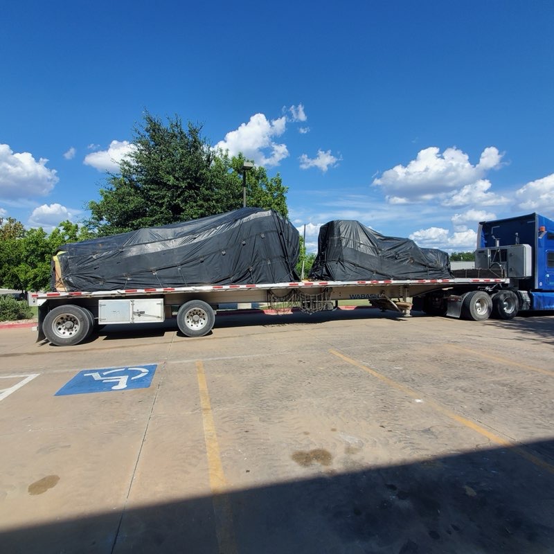 Two tarped machinery loads secured on a Wabash flatbed behind a blue Kenworth tractor